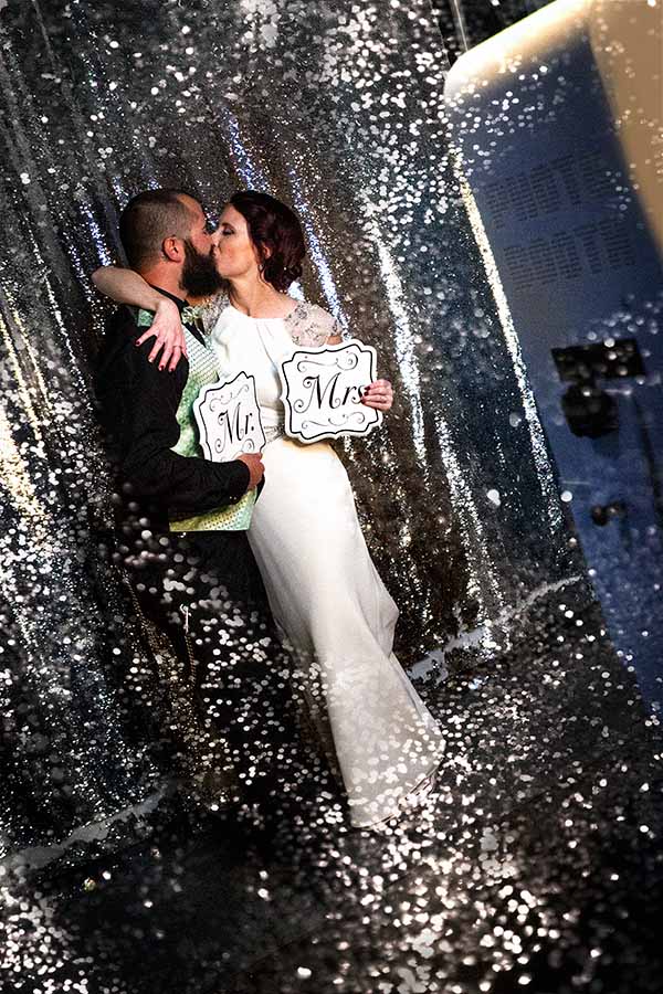 wedding_couple_shiny_sparkles_booth Couple Kiss in the photo booth standing in a silver shiny sequin backdrop at a wedding in Luther, Oklahoma.